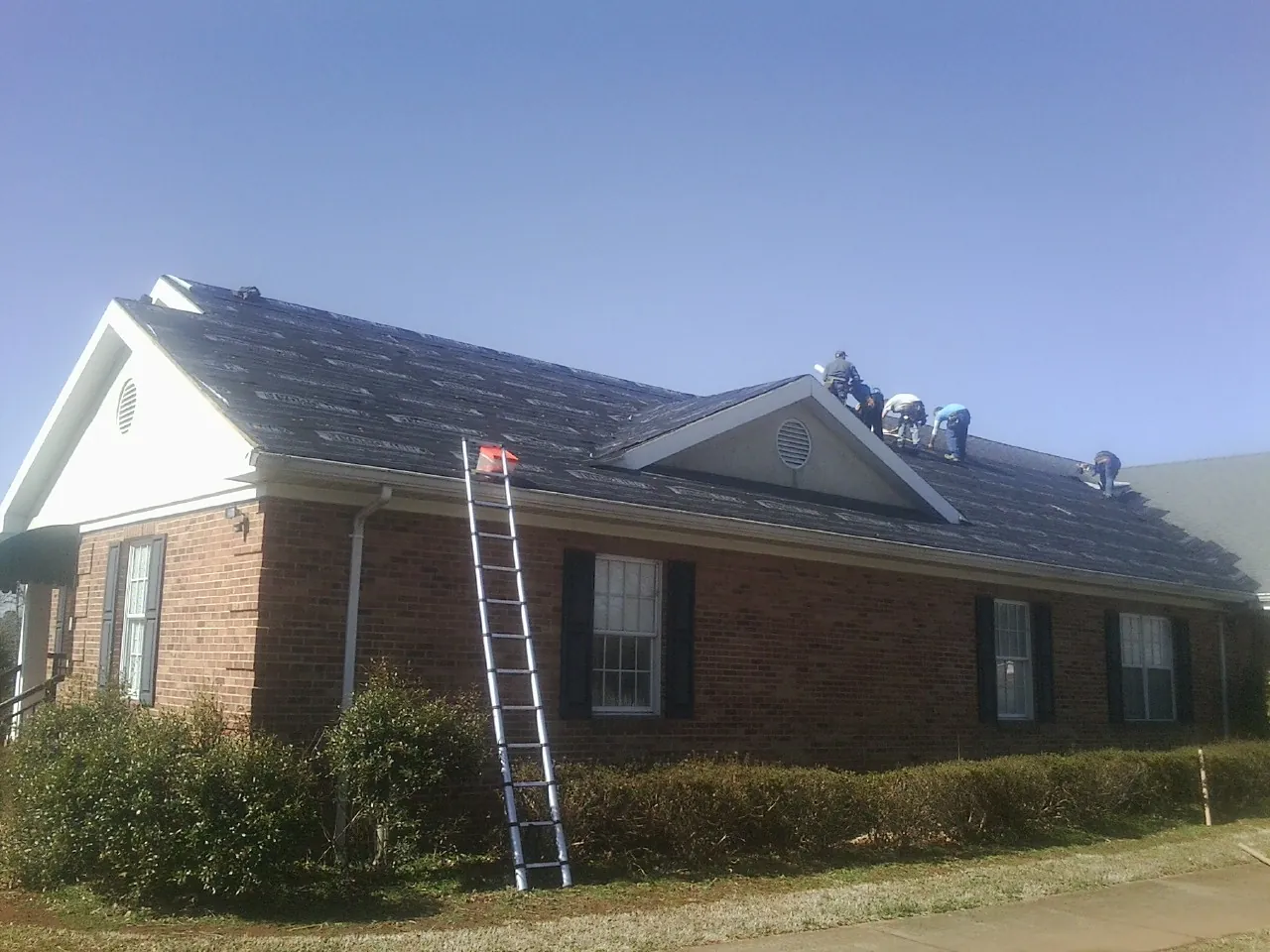 Crew tearing shingles off a brick ranch roof with a ladder set — Metal Roof Repair work by our crew in Olivehill