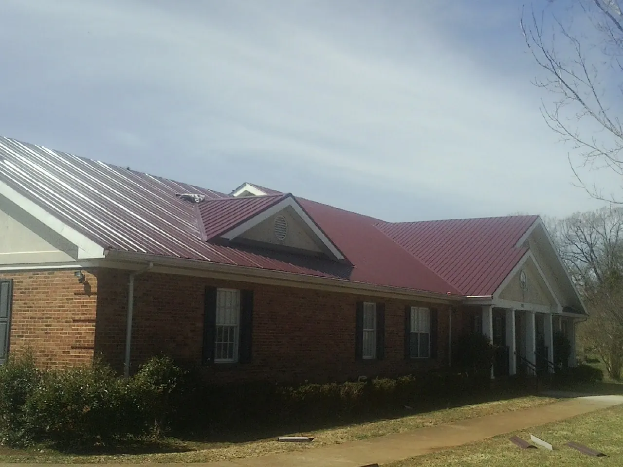 Red metal roof with gabled entries on a long brick building, from a Hail Damage Roof Repair job in Olivehill