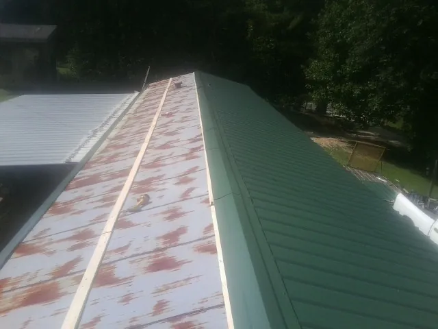 Old rusted panels beside newly installed green metal roofing — Wind Damage Roof Repair by Roofing Brothers in Olivehill