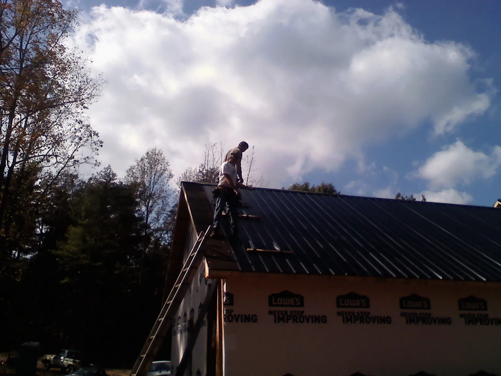 Roofer fastening dark metal panels high against a cloudy sky, from a Roof Inspection job in Olivehill