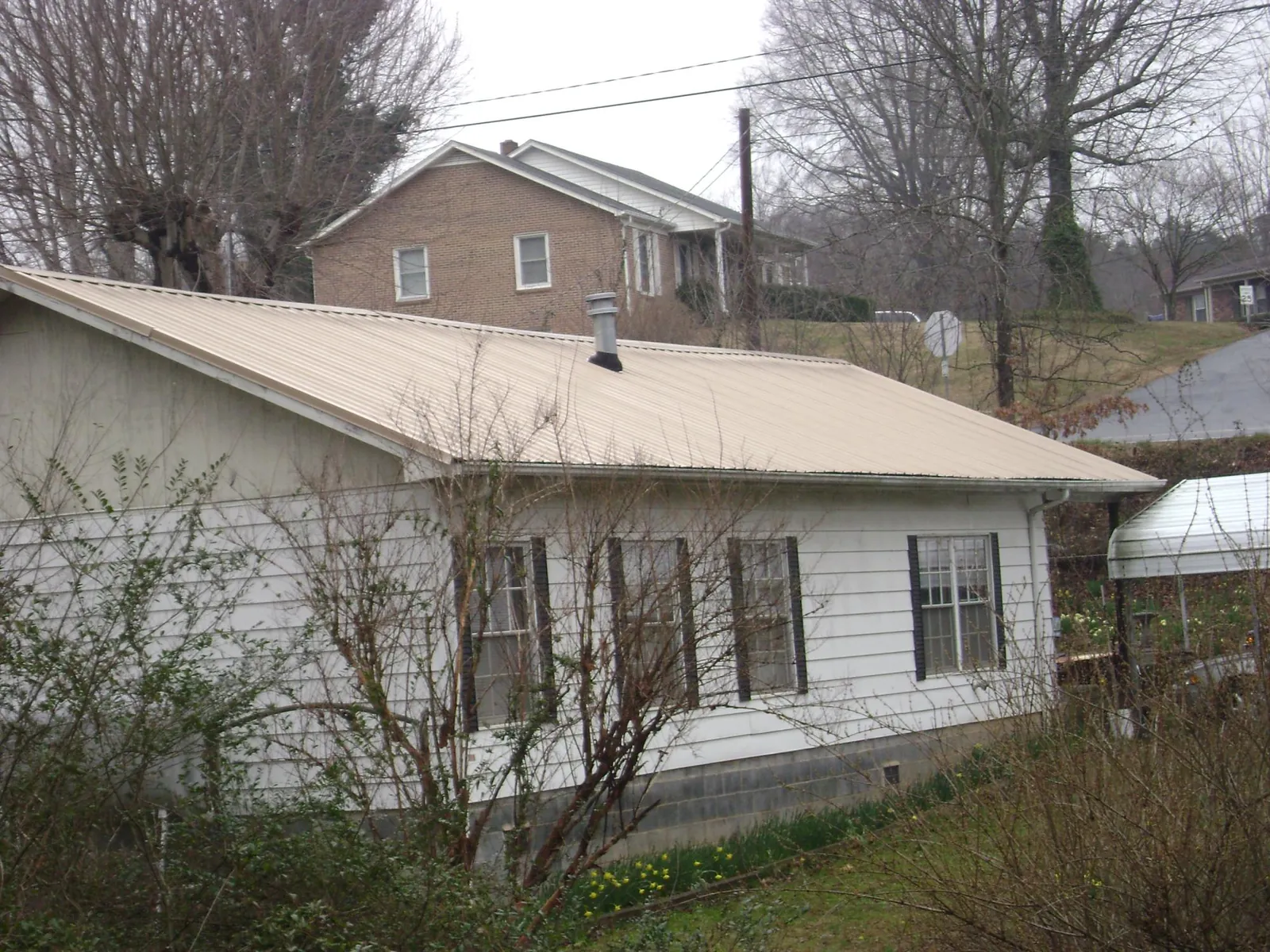 Tan metal roof on a white sided house set into a hillside — Commercial Roofing by Roofing Brothers in Olivehill
