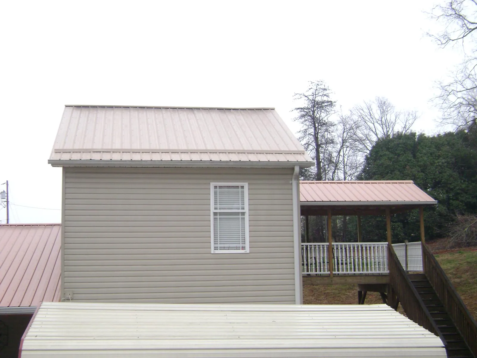 Tan metal roofs on a two story addition and attached porch, from a Roof Replacement job in Olivehill